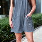 Person wearing a gray sleeveless dress with pockets outdoors.